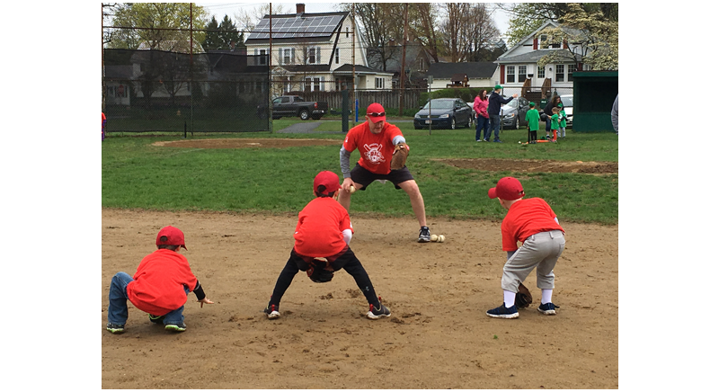 a baseball coach giving instructions about fielding the ball to three kids